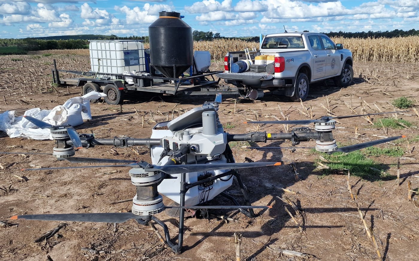 Kunz Agrotech's DJI Agras T100 on a harvested field in Uruguay, with the support vehicle and a trailer with water tank and mixing equipment.